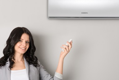 Une dame commande son climatiseur haut mural gris à distance grâce à une télécommande
